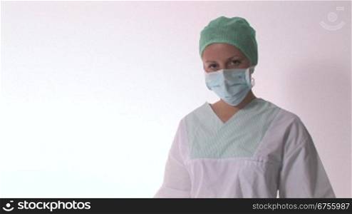 Eine Krankenschwester nimmt ihren Mundschutz weg, verschrSnkt die Arme und lSchelt