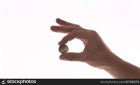 Eine Person hSlt eine Euro Mnnze zwischen Daumen und Zeigefinger und spielt damit