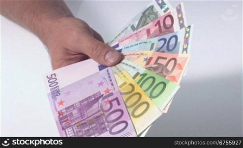Eine Person hSlt mehrere Euro Geldscheine in der Hand und zieht dann die Hand aus dem Kamera-Blickwinkel