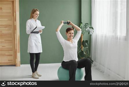 elder woman covid recovery doing physical exercises with dumbbell while nurse checks