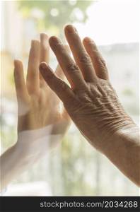 elder woman touching hand with someone through window during pandemic