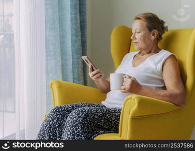 elder woman using smartphone home during pandemic while having coffee