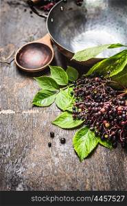 Elderberries for cooking with spoon and vintage pot on rustic wooden background