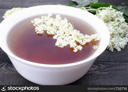 Elderberry tea with flowers on a wooden table. Healthy Medicine Elderberry Flower Tea. Elderberry tea with flowers on a wooden table.
