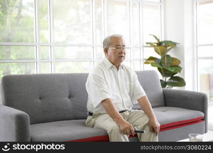 Elderly Asian man watching television sitting on a sofa in the living room at home, retirement concept