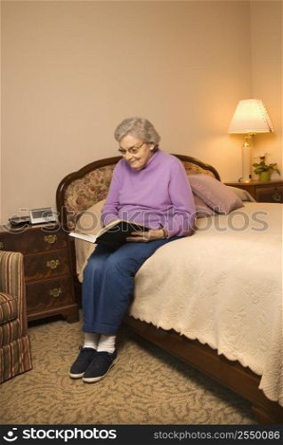 Elderly Caucasian woman in bedroom at retirement community center reading a book.