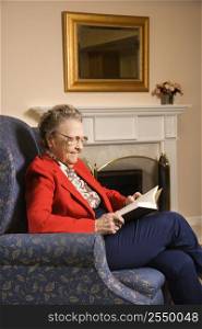 Elderly Caucasian woman reading book in chair at retirement community center.