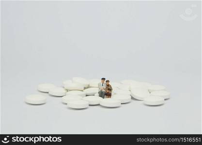 Elderly couple figure sitting on a pile of white pills.