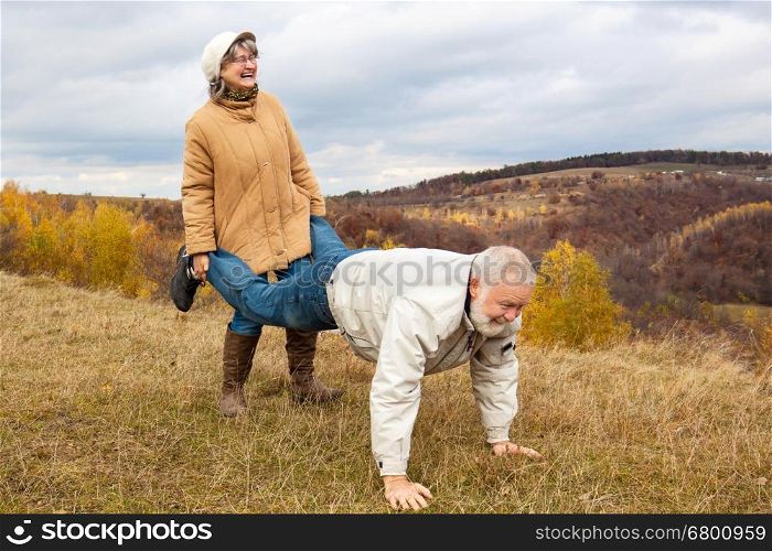 Elderly couple having fun and playing the wheelbarrow in nature.