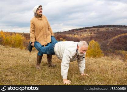 Elderly couple having fun and playing the wheelbarrow in nature.