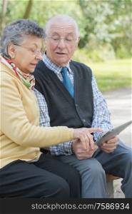 elderly couple in the park with a tablet