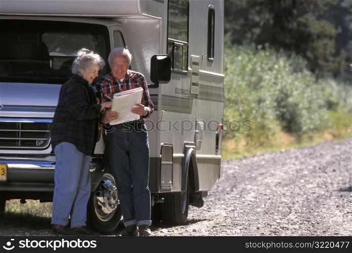 Elderly Couple Looking At Map While Standing Next To Motor Home