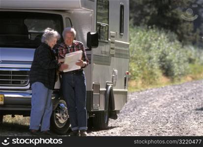Elderly Couple Looking At Map While Standing Next To Motor Home