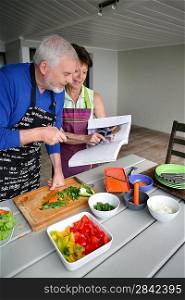 Elderly couple preparing a meal with the help of a cookbook