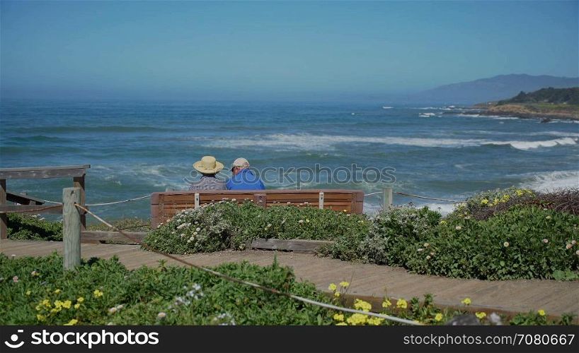 Elderly couple sit on bench in view of ocean