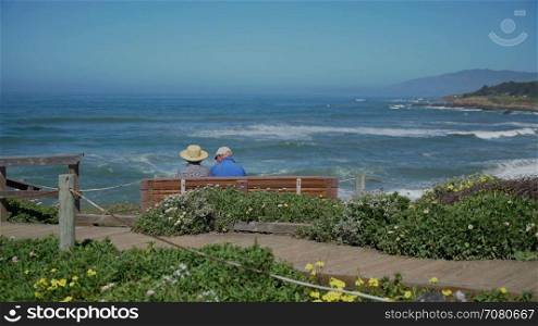 Elderly couple sit on bench in view of ocean