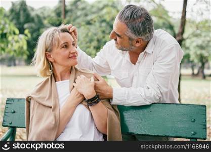 Elderly couple sitting on a bench showing love together at the public park in the morning. Happy concept of lifestyle in the retirement
