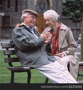 Elderly Couple Sitting On Park Bench And Smiling