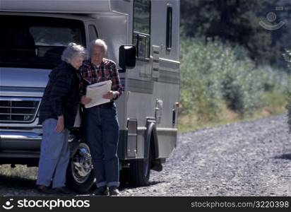 Elderly Couple Standing Next To RV And Looking At Map