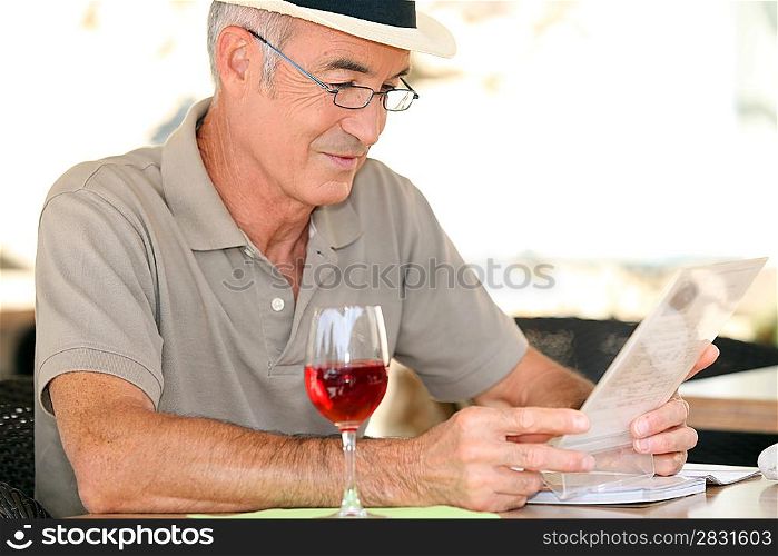 elderly gentleman seated in cafe drinking glass of red wine
