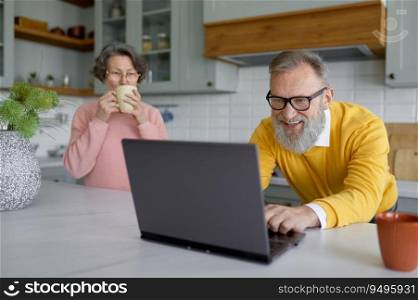 Elderly husband enjoying video game on laptop while old wife drinking coffee in need of attention. senior couple relationships and gadget addiction concept. Elderly husband enjoying video game on laptop while old wife drinking coffee