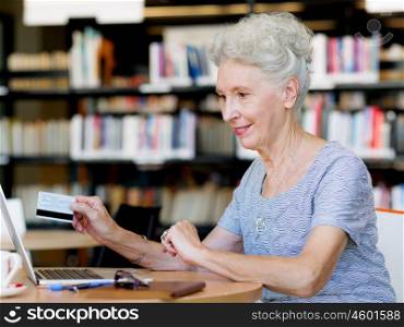 Elderly lady holding a card and working with laptop. Shopping online