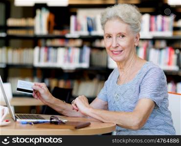 Elderly lady holding a card and working with laptop. Shopping online