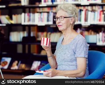 Elderly lady in the libary with cup of tea. Few minutes for tea
