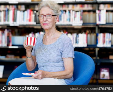 Elderly lady in the libary with cup of tea. Few minutes for tea