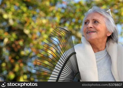 Elderly lady raking leaves in her garden