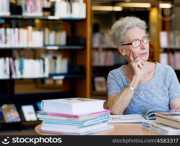 Elderly lady reading books in library. Taking her time with new books