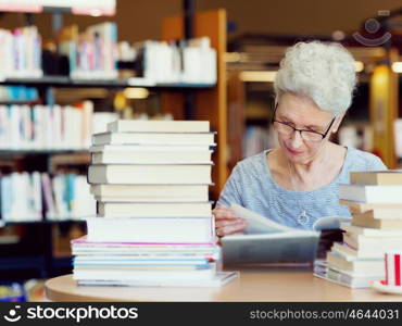 Elderly lady reading books in library. Taking her time with new books