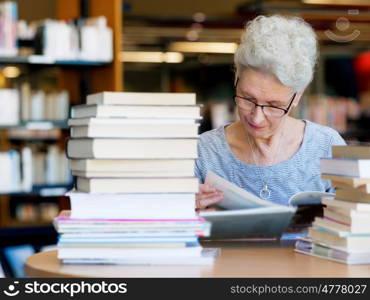 Elderly lady reading books in library. Taking her time with new books