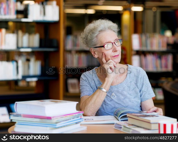 Elderly lady reading books in library. Taking her time with new books