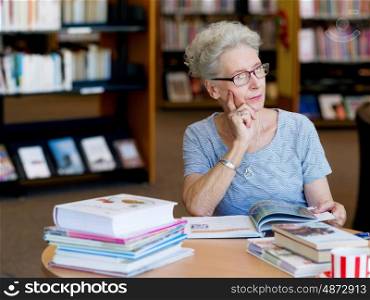 Elderly lady reading books in library. Taking her time with new books