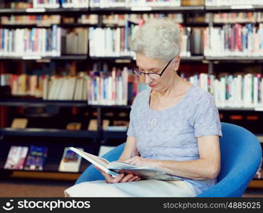 Elderly lady reading books in library. Taking her time with new books