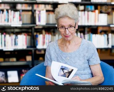 Elderly lady reading books in library. Taking her time with new books