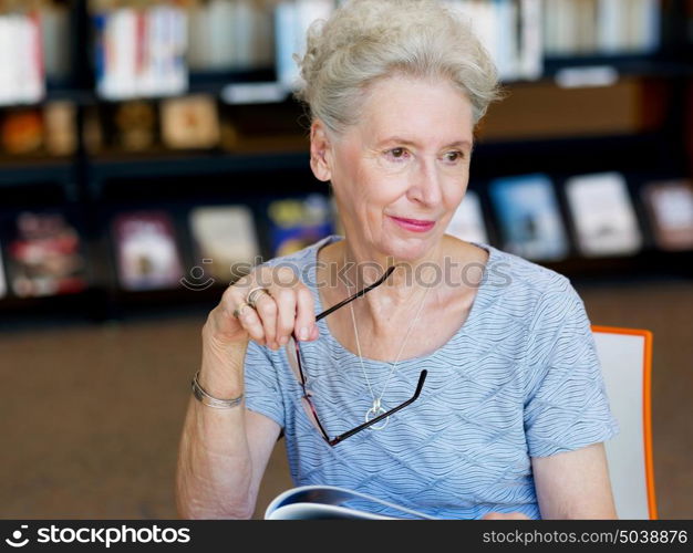 Elderly lady reading books in library. Taking her time with new books