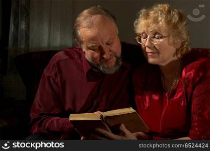 Elderly man and woman reading the book on a dark background. Happy elderly spouses behind reading