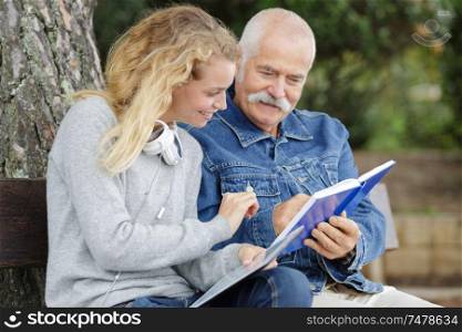 elderly man and young woman looking at book outdoors