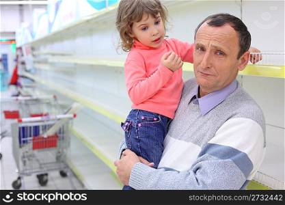 elderly man at empty shelves in shop with child on hands