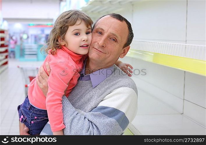 elderly man at empty shelves in shop with child on hands