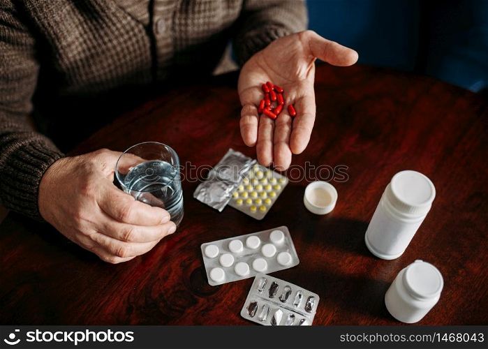 Elderly man hand with pills, home office on background, age-related diseases. Mature senior is ill and being treated in his house. Elderly man hand with pills, age-related diseases