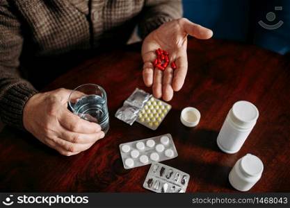 Elderly man hand with pills, home office on background, age-related diseases. Mature senior is ill and being treated in his house. Elderly man hand with pills, age-related diseases