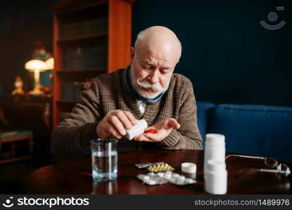 Elderly man hand with pills, home office on background, age-related diseases. Mature senior is ill and being treated in his house. Elderly man hand with pills, age-related diseases