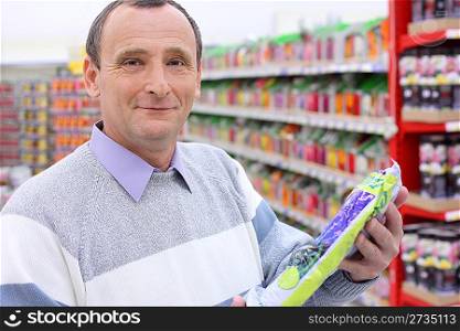 elderly man in shop with package in hands, looking at camera
