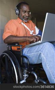 Elderly man in wheelchair listening to music and using laptop