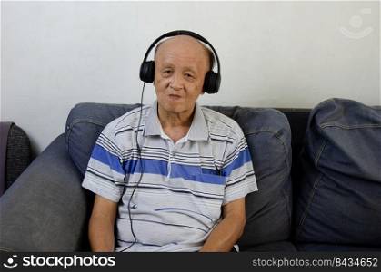 elderly man listening to music with headphones on the sofa.