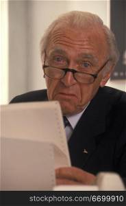 Elderly Man Looking At Printouts And Frowning