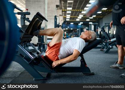 Elderly man on exercise machine, gym interior on background. Sportive grandpa on fitness training in sport center. Healty lifestyle, health care, old sportsman. Elderly man on exercise machine in gym